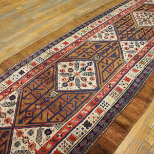 Navy, red, and cream geometric runner rug displayed diagonally on distressed yellow wood floorboards.
