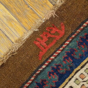 The rug's brown backing and multicolored geometric borders lie against light, distressed wood plank flooring.