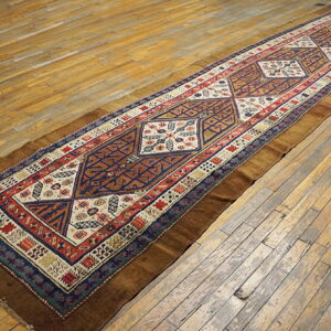 A long runner with a geometric pattern in navy, red, and brown lies on natural wood planks.