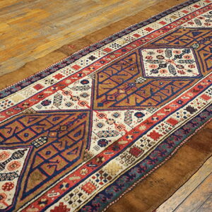 Geometric runner in brown, navy, red, and ivory laid diagonally across worn wooden floorboards.