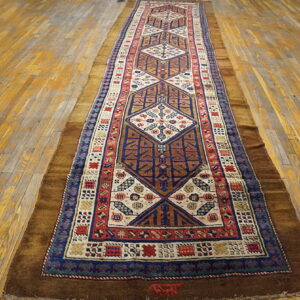 A narrow rug featuring repeating diamond patterns in blue, cream, and red on golden plank flooring.