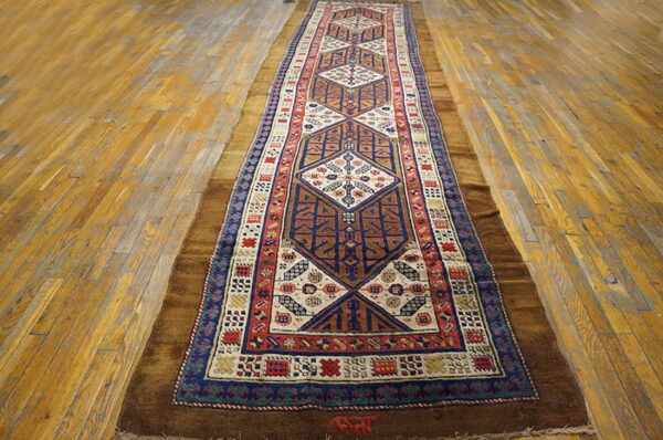 A narrow rug featuring repeating diamond patterns in blue, cream, and red on golden plank flooring.