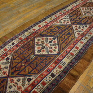 Low-pile runner rug with complex geometric motifs in blue, red, cream, and brown on rustic wood flooring.