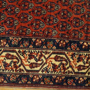 Low-pile red rug detail with dense navy and cream traditional patterns near wood floor.