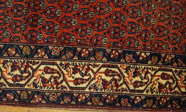 Low-pile red rug detail with dense navy and cream traditional patterns near wood floor.