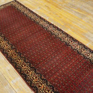 Red runner rug featuring a detailed pattern and gold border laid on light-colored wood flooring.