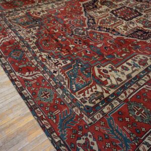 Traditional red, blue, and cream patterned rug partially covers distressed light wood flooring.