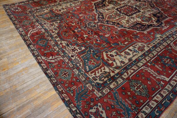 Traditional red, blue, and cream patterned rug partially covers distressed light wood flooring.
