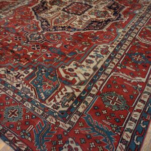 Red rug with detailed blue and cream geometric patterns partially covers worn wooden flooring.