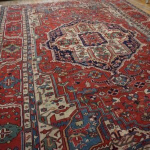 Large low-pile red rug with detailed navy and cream medallion pattern on worn wood floors.