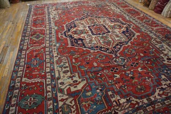 Large low-pile red rug with detailed navy and cream medallion pattern on worn wood floors.