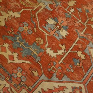Worn rust rug texture showing blue, cream, and red geometric and stylized floral patterns.