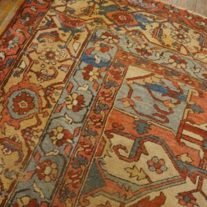 A low-pile rug featuring complex floral and geometric patterns in rust, blue, and tan on a wood floor.