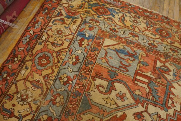 A low-pile rug featuring complex floral and geometric patterns in rust, blue, and tan on a wood floor.