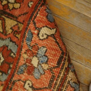 Close-up showing the terracotta, blue, and tan patterned rug folded on yellow wood planks.