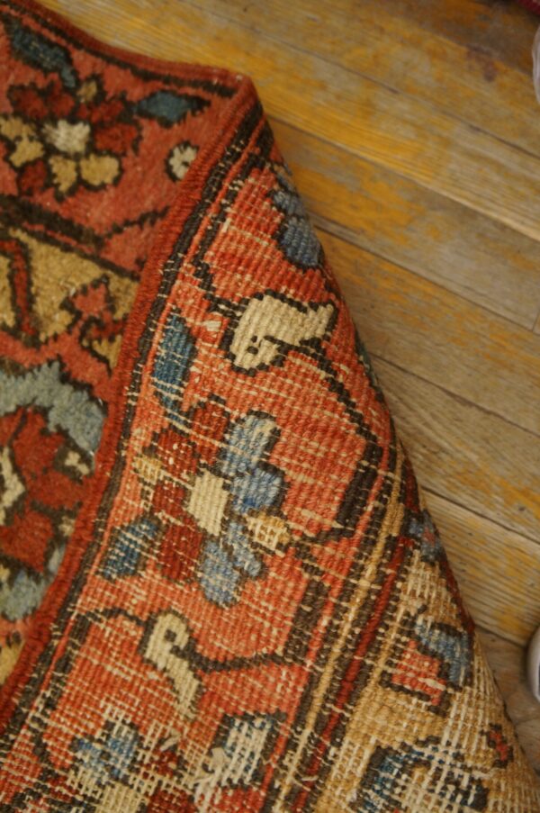 Close-up showing the terracotta, blue, and tan patterned rug folded on yellow wood planks.