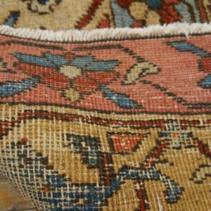 Close-up of a pink, blue, and tan patterned rug folded to show its tight woven backing on wood flooring.