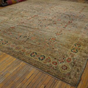 Ornate floral rug in muted sage green and terracotta colors rests on wide wood plank flooring.