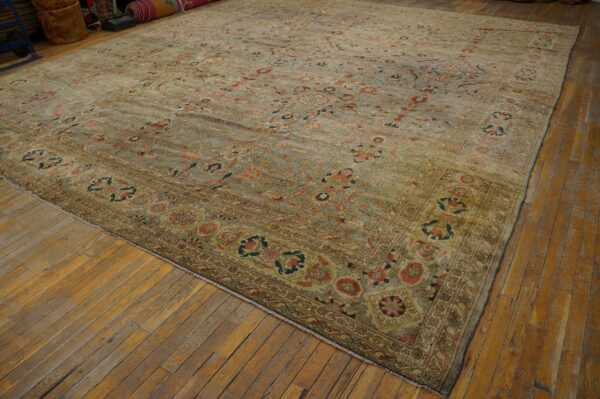 Ornate floral rug in muted sage green and terracotta colors rests on wide wood plank flooring.