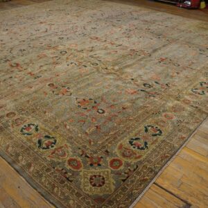 A large, distressed area rug with a muted sage and coral floral pattern lies on wide plank wood flooring.