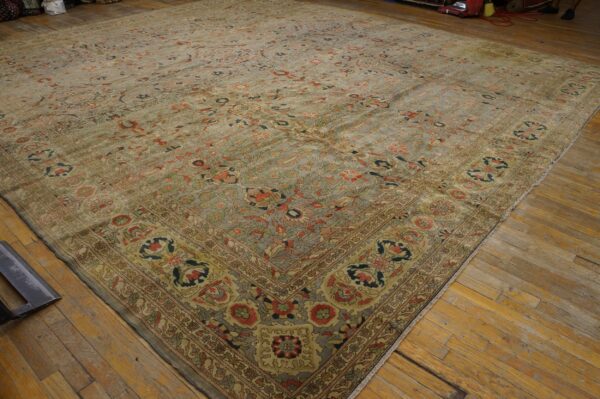 A large, distressed area rug with a muted sage and coral floral pattern lies on wide plank wood flooring.