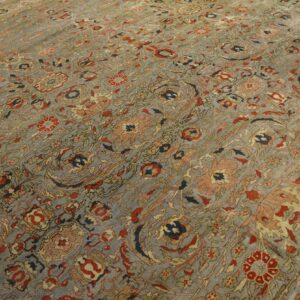 Detail of a low-pile rug with an ornate floral pattern in muted gray, red, and navy on a hardwood floor.