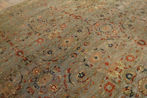 Detail of a low-pile rug with an ornate floral pattern in muted gray, red, and navy on a hardwood floor.