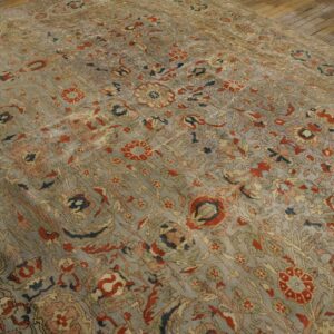 Faded slate blue rug with an intricate all-over floral pattern in red, peach, and olive green on wood flooring.