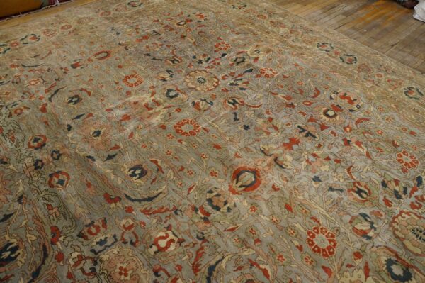 Faded slate blue rug with an intricate all-over floral pattern in red, peach, and olive green on wood flooring.