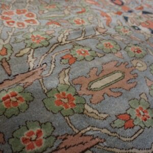 Close-up of a medium pile rug featuring coral and green floral motifs on a muted blue field.
