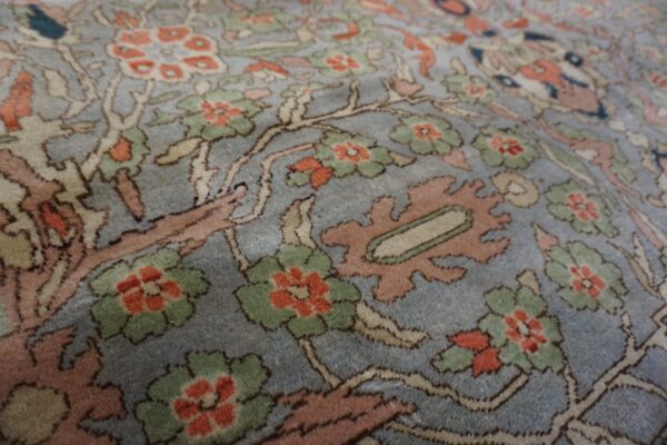 Close-up of a medium pile rug featuring coral and green floral motifs on a muted blue field.