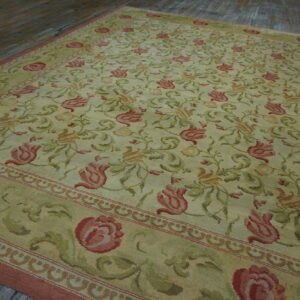 Pale green rug with extensive red and olive green floral and vine motifs displayed on wooden flooring.