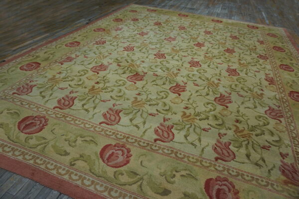 Pale green rug with extensive red and olive green floral and vine motifs displayed on wooden flooring.