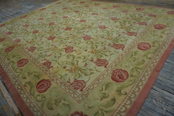 Sage green and cream rug with a dense pink and red floral design resting on weathered wood floorboards.