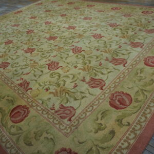 Pale green and red floral pattern rug with wide border displayed on rustic gray wood flooring.