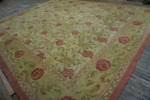Pale green and red floral pattern rug with wide border displayed on rustic gray wood flooring.