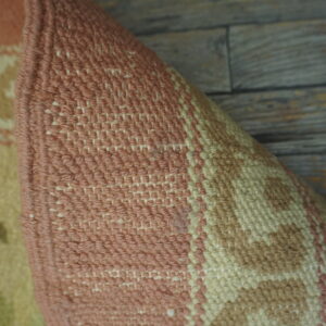 Pink, cream, and tan patterned rug texture resting partially rolled against weathered gray wood planks.