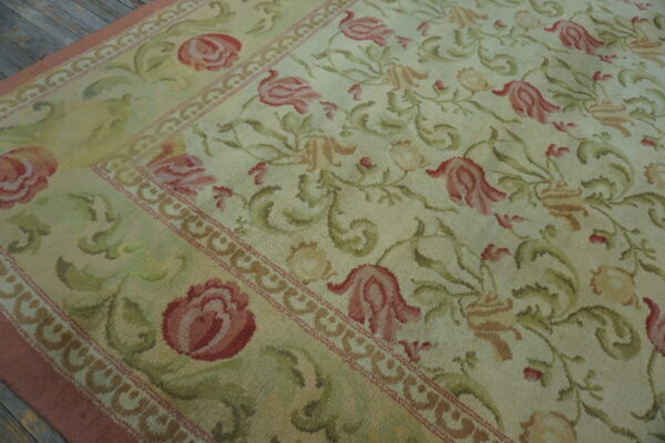 Floral vine rug in shades of cream, rose, and pale green, showing a decorative border on wood planks.