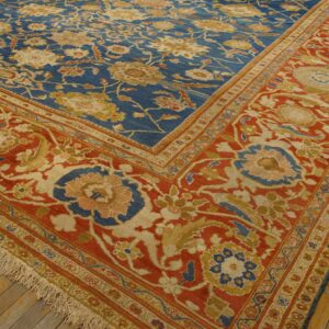 Ornate blue and red patterned rug with gold and cream motifs laying on distressed wood flooring.
