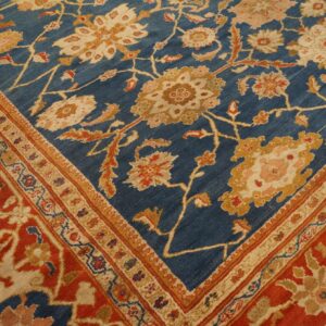 Ornate floral rug corner displaying a deep blue field bordered by rust red and cream patterns.