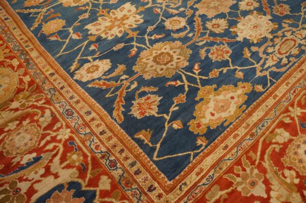 Ornate floral rug corner displaying a deep blue field bordered by rust red and cream patterns.