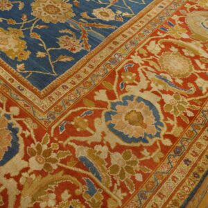 Blue and red traditional floral rug with gold and cream accents rests on rustic wood flooring.