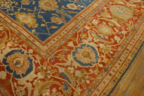Blue and red traditional floral rug with gold and cream accents rests on rustic wood flooring.