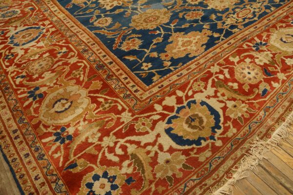 Blue and rust floral rug corner, showing detailed border patterns and beige fringe on wood floor.