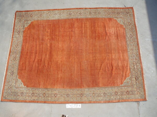 Rust orange rug with a solid field and traditional border in pale blue and tan is displayed on gray concrete.