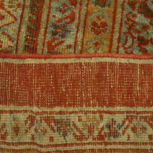 High pile rug texture featuring rust red, blue, and green patterns adjacent to a tightly woven flat area.