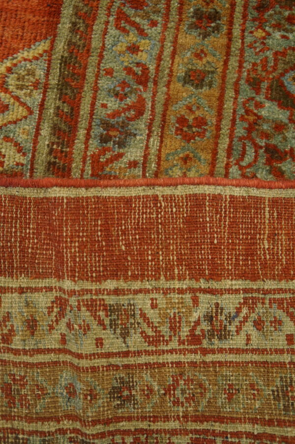 High pile rug texture featuring rust red, blue, and green patterns adjacent to a tightly woven flat area.