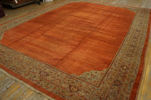 Burnt orange area rug with a streaked field and intricate border of green, teal, and brown florals.