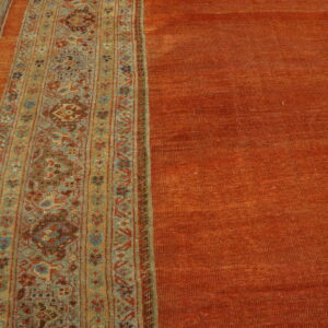 Textured orange rug with a patterned teal, gold, and red stripe placed next to worn yellow wood planks.