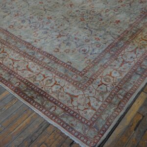 Ornate, low-pile rug in pale blue, beige, and rust colors rests on worn hardwood planks.
